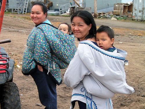 Two Inuit women carrying their children in the traditional fashion, in the hoods of their parkas
