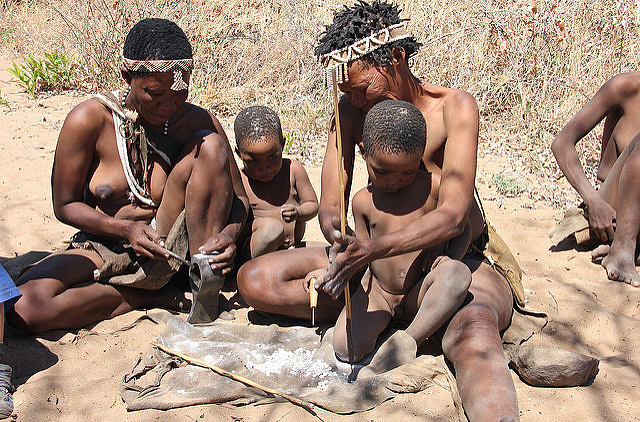 Adult Ju/’hoansi teaching children one of their traditional cultural practices, making beads our of ostrich egg shells 