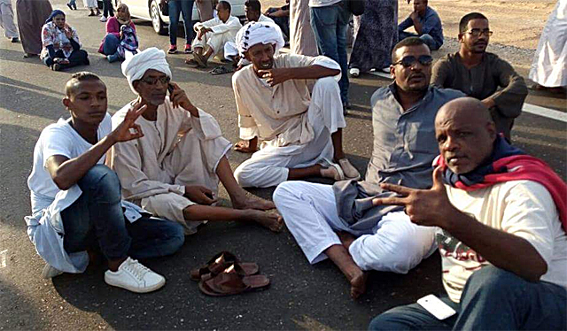 Nubian protesters sitting on the Aswan to Abu Simbel highway, November 2016, men in the foreground and some women in the background (Photo from the news blog Egyptian Chronicles, Creative Commons license)