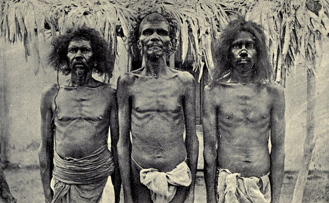 Three Yanadi men behind whom is a mud-walled house 