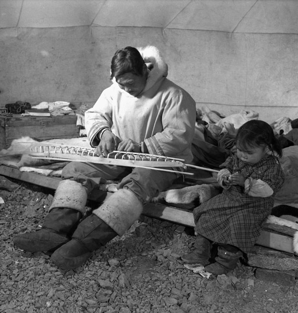 An Inuit man, Salomonie, working on a model kayak for the Canadian Handicrafts Guild, with his daughter, Annie, at his side 