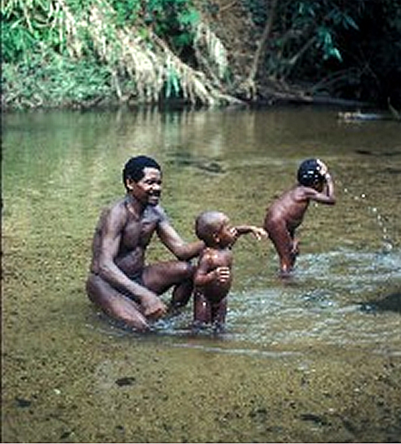 Batek man bathing two of his kids in a stream, a tributary of the Lebir River in Malaysia